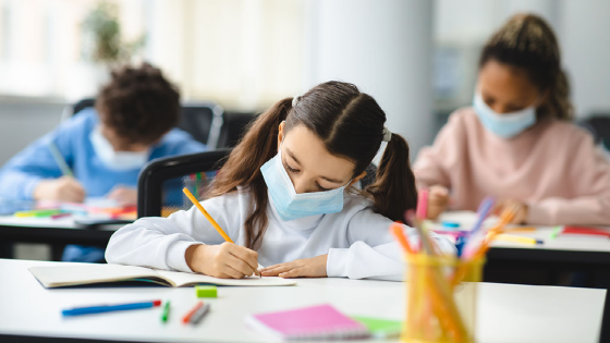 Student wearing a protective mask writes on a paper in a classroom