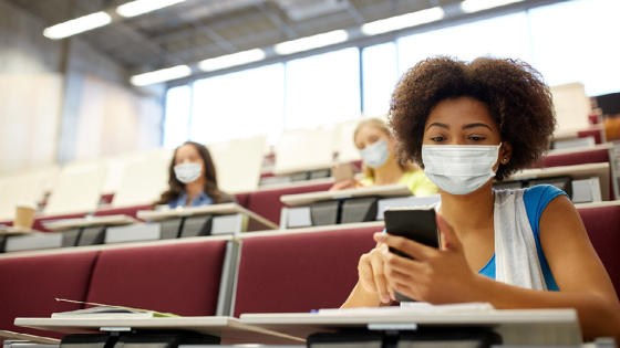 Student wearing protective mask looks at her phone in lecture hall