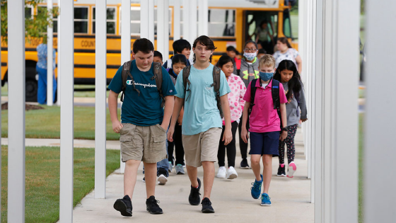 Students arriving by bus walk down a covered entryway