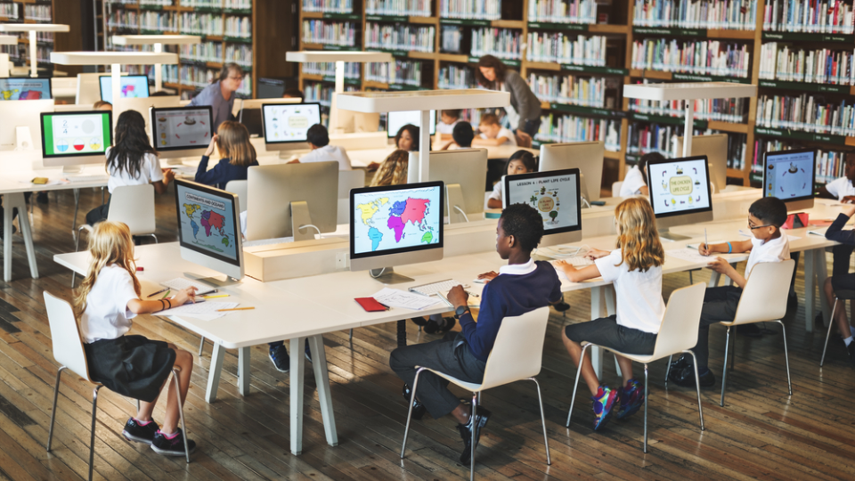 Students in a school library work on computers.