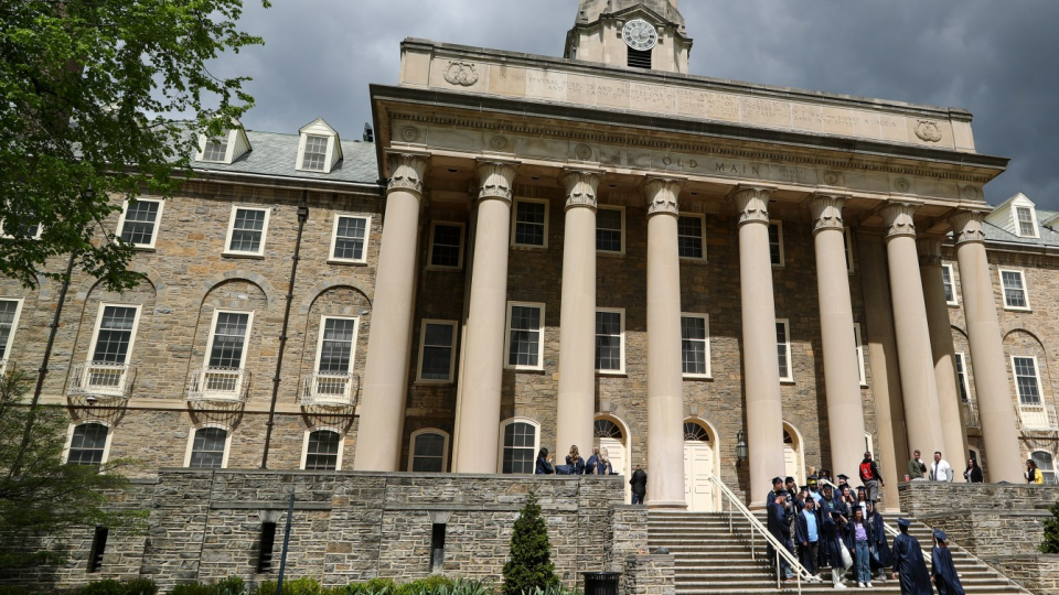 Students in caps and gowns pose for photos on the steps of Old Main on the campus of Penn State University in State College, Pa.