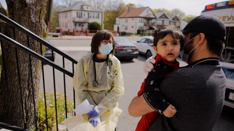 Syed Kamal holds his daughter outside their home as Boston Medical Center pediatrician Dr. Sara Stulac does a routine check-up