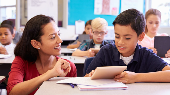 Teacher helping elementary school boy using tablet computer