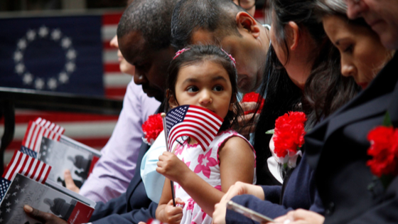 The daughter of a immigrant holds an American flag while she joins her mothers naturalization ceremony