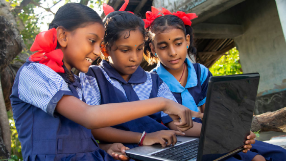 Three girls in a rural town in India use a laptop for school