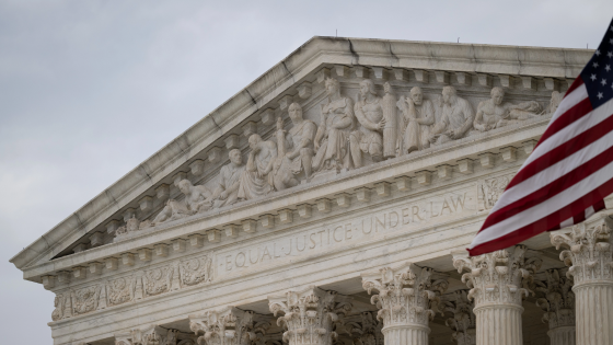 Top of Supreme Court building with American flag flying in front of it