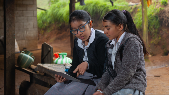 Two Colombian girl students doing their homework with a digital tablet at home.