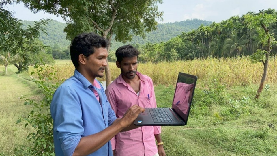 Two men look at laptop in the middle of rural area