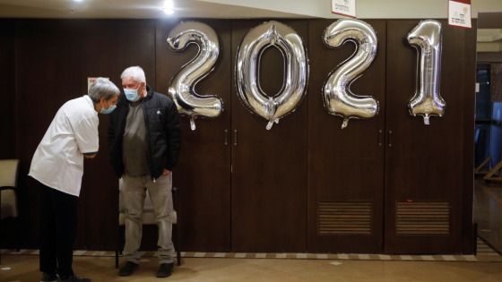 Two men standing next to 2021 balloons