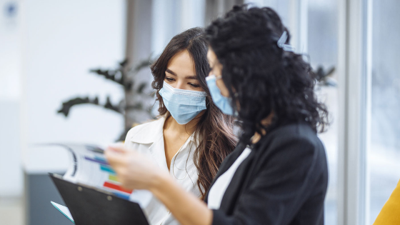 Two women checking charts and discussing business trends in the office