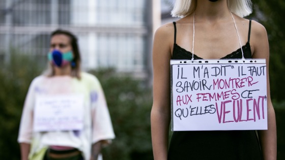 Two women wear placards around their neck featuring the testimony of victims of sexual assault