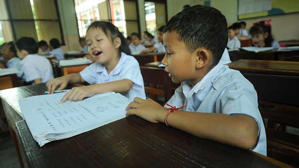 Two young students read a school textbook in class together.