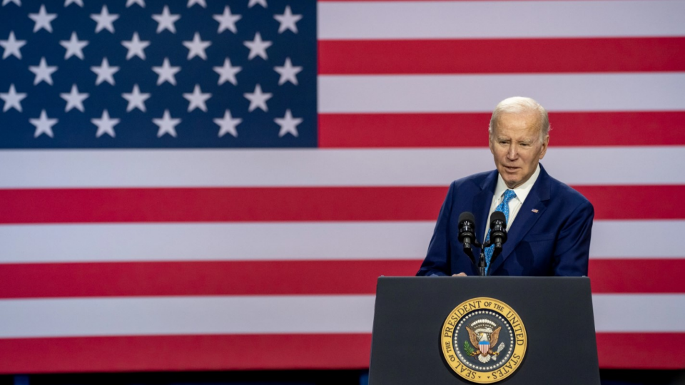 U.S. President Joe Biden speaks at podium with flag displayed behind him