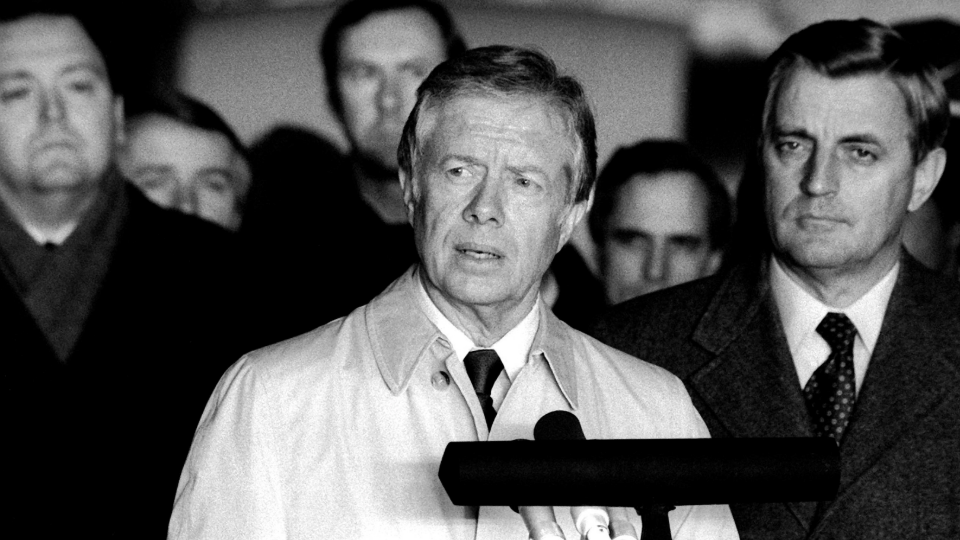 Upon their arrival at the base after their release from Iran, the former hostages and former Vice President Walter Mondale listen as former President Jimmy Carter speaks to the crowd