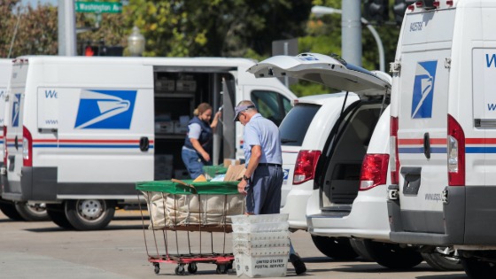 USPS workers load mail into delivery trucks