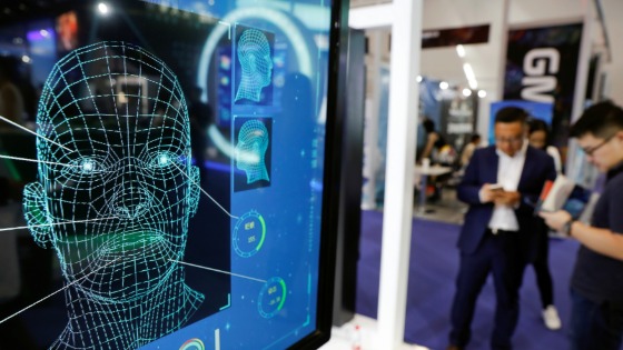 Visitors check their phones behind the screen advertising facial recognition software