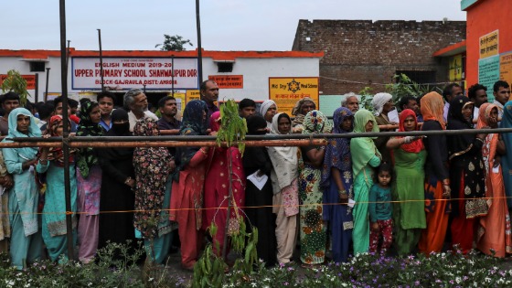 Voters line up to cast their votes outside a polling station during the second phase of general election in Amroha