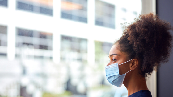 Woman looking out window with mask during pandemic.