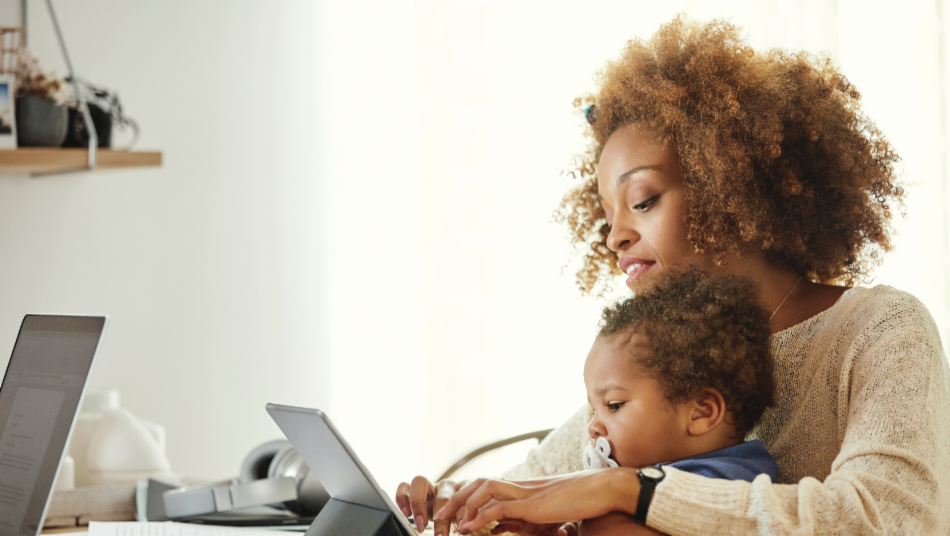 Mother using wireless computer while holding son at table.