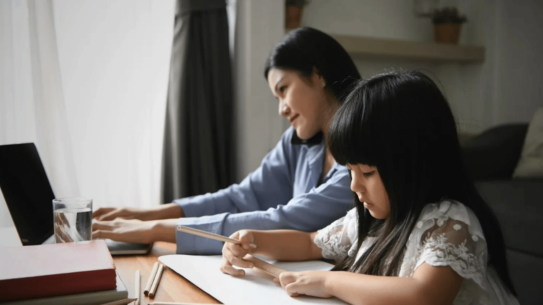 Woman working with child doing homework next to her