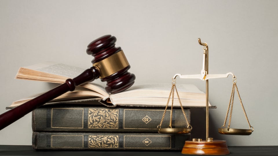 Wooden judge gavel, law scales and stack of books on table in a courtroom.