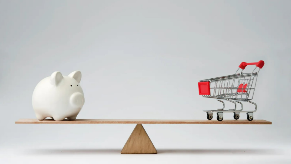 Wooden seesaw with piggy bank on one side and grocery cart on another