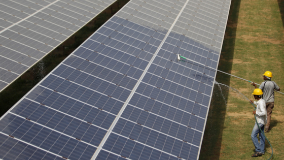 Workers clean photovoltaic panels inside a solar power plant in Gujarat
