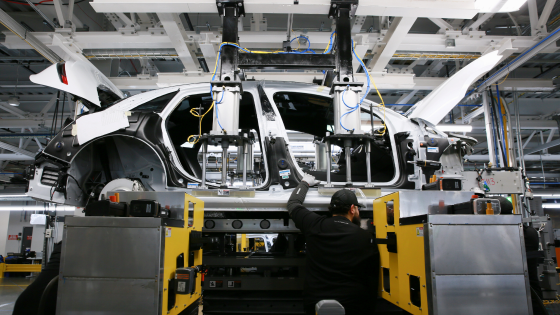 Workers marry the body structure with the battery pack and the front and rear sub frames as they assemble electric vehicles