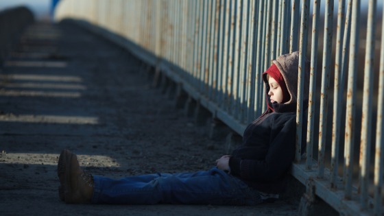 Young boy sleeping against a metal fence