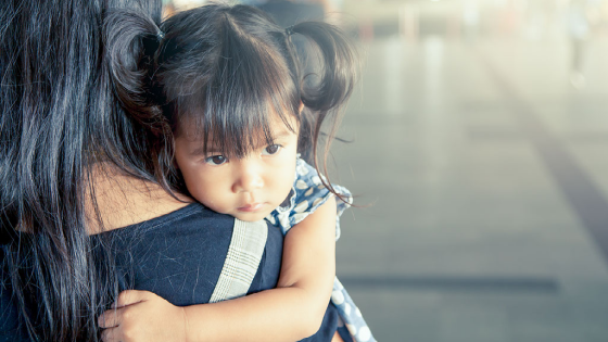 Young girl being carried by her mother at a train station