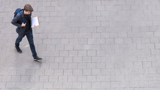 Young man walks to class with a backpack and notebook