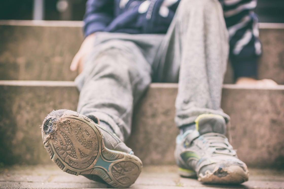 A child sitting on steps wearing old sneakers with holes in them.