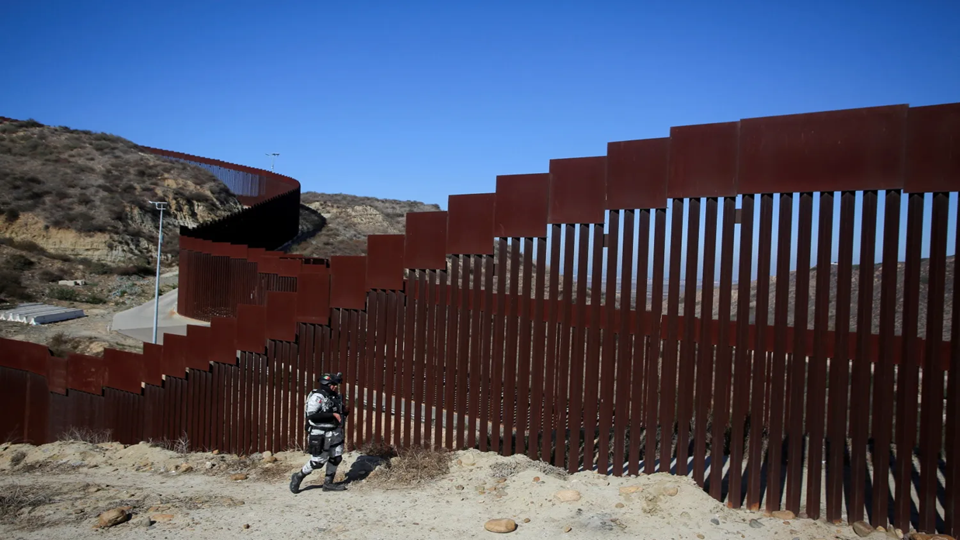 Image depicting a member of Mexico's National Guard patrols the border wall between Mexico and the U.S. after Mexican President Claudia Sheinbaum agreed with U.S. President Donald Trump to bolster border enforcement efforts in response to Trump's demand to crack down on immigration and drug smuggling, in Tijuana, 